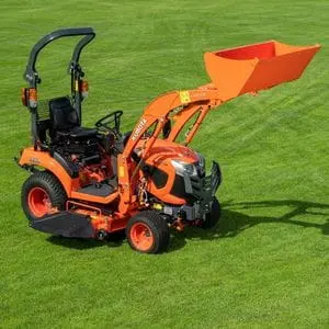 a Kubota miniature tractor fitted with a front loader, mowing deck and rollover protection structure, parked on a lawn