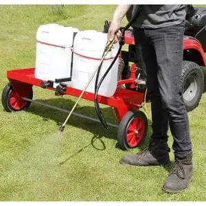 a man stood behind a red ride-on mower, using a spray lance from the SCH HGPS Sprayer attachment