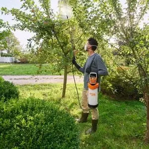 a man wearing a protective mask, stood in an orchard, spraying a tree using the STIHL SGA 30 Cordless Sprayer