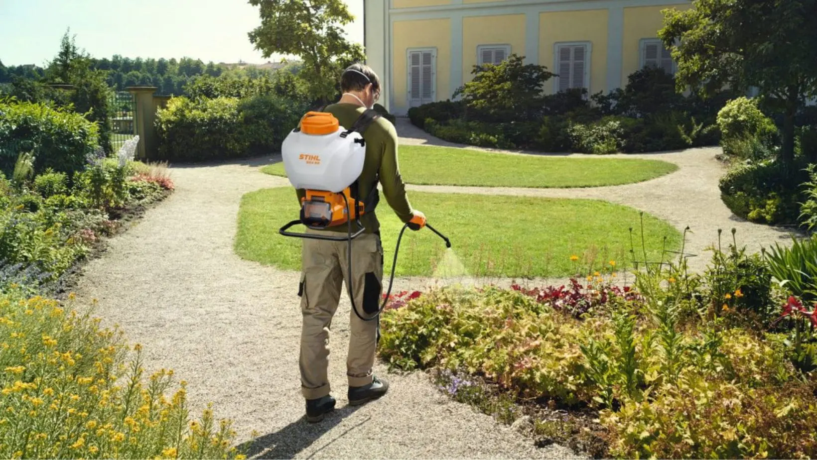 a man spraying plants in a flowerbed outside a stately home, using the STIHL SGA 60 Cordless Sprayer