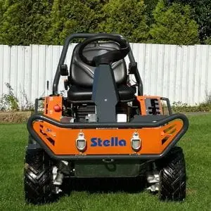 the Stella Racoon 95 4x4 Ride-On Flail Mower parked on a lawn, with a white picket fence and trees in the background