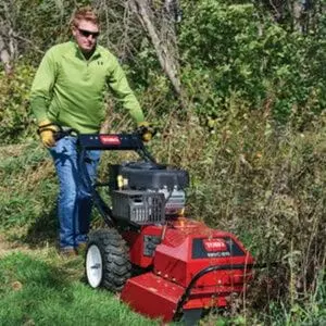 a man cutting down scrub at the edge of a field, using the Toro Brush Cutter BRC-28