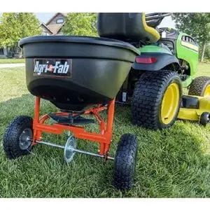 a green garden tractor towing the AGRI-FAB 45-0527 Towed Spreader across a lawn