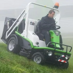a man cutting grass down a steep hill, in overcast weather, using the Etesia 124DX Hydro Ride-on Mower