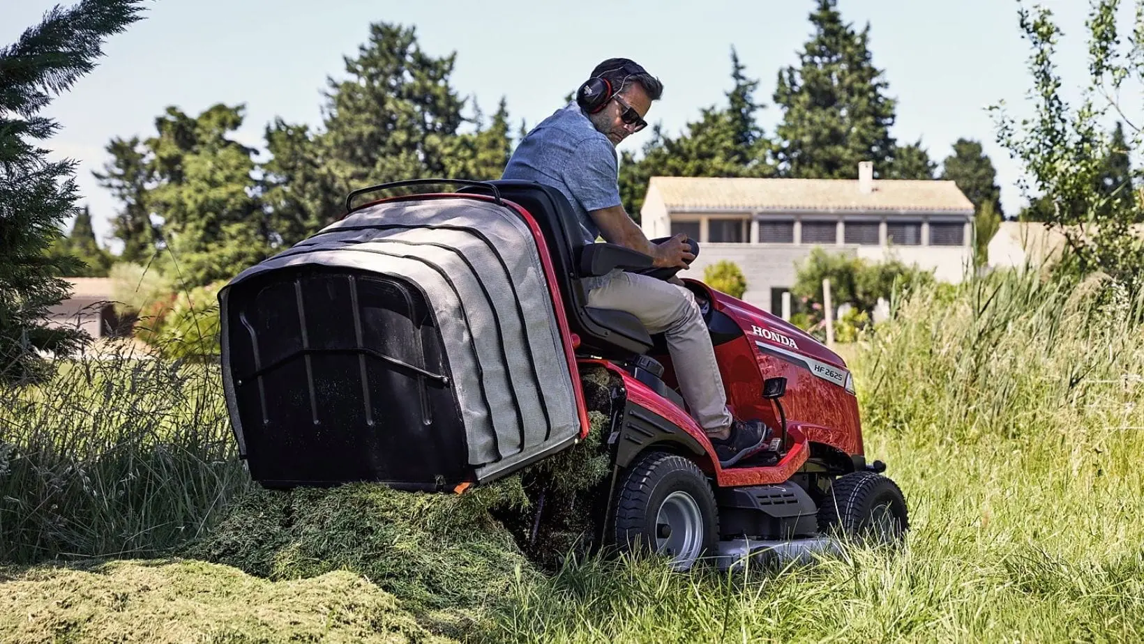 Honda HF Ride On Mower (1) a man using a Honda HF Ride On Mower's low-dump grass collector to deposit grass at the edge of a field