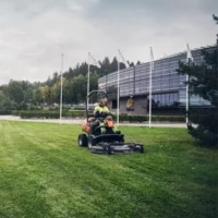 a man using the Husqvarna P 520DX Out Front Mower to cut grass outside a large commercial premises