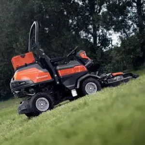 the Husqvarna P 524XR EFI Out Front Mower parked on a steep grassy hill, in front of some trees