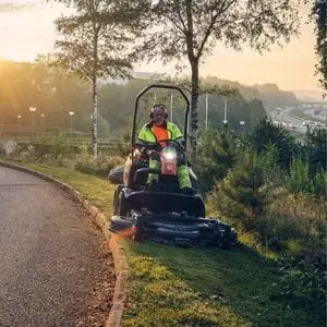 a man wearing a high-visibility jacket, using the Husqvarna P 525DX Out Front Mower to cut a thin strip of grass at a roadside