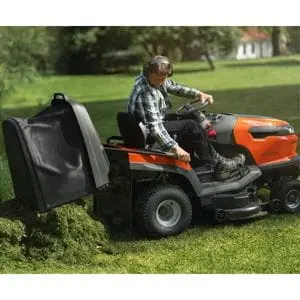 a man sat in the driver's seat of a Husqvarna Tractor 200 Series ride-on mower, emptying clippings from the collector box onto the edge of a large lawn