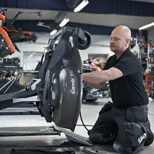 a service technician in a workshop, working on a riding mower's combi deck