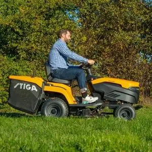 a man cutting and collecting grass in a field using a STIGA battery garden tractor