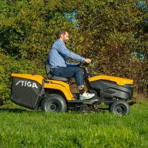 a man cutting grass near some trees, using the STIGA Estate 598e Battery Garden Tractor