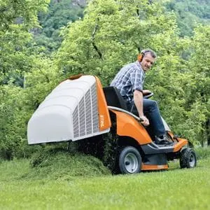 a man sat on the STIHL RT 4082 Petrol Ride-on Lawn Mower, operating the grass collector dumping system at the edge of a lawn