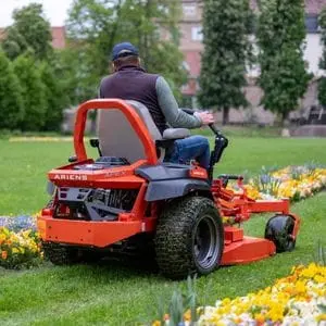 a man mowing a lawn between flowerbeds, using the Ariens Apex 48R Zero Turn Mower