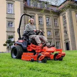 a man mowing a sloping lawn outside a stately home, using the Ariens Zenith 52R Zero Turn Mower