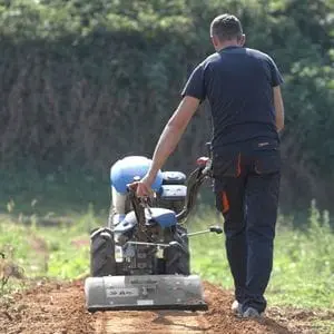 a rearview shot of a man working agricultural ground using the BCS 706 PowerSafe®2 Wheel Tractor equipped with a rotary hoe attachment