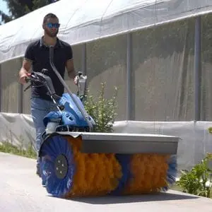 a man wearing sunglasses, using the BCS 706 PowerSafe®2 Wheel Tractor with sweeper attachment on a concrete path