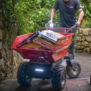 a man manoeuvring a Bluebird WB 500 E Electric Power Barrow full of compost bags along a narrow path