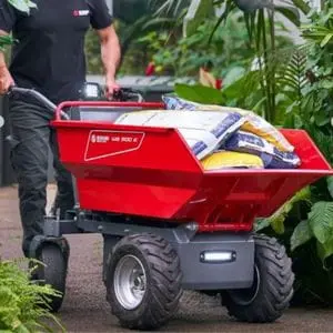 a man pushing the Bluebird WB 500 E Electric Power Barrow, loaded with compost bags, along a path lined with plants