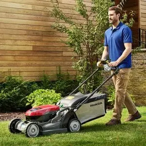 a man wearing a blue polo shirt and beige chinos, using a Honda HRX mower to mow a lawn