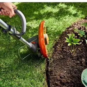 the Husqvarna 110iL FLXi Grass Trimmer cutting a lawn edge next to a circular flower bed