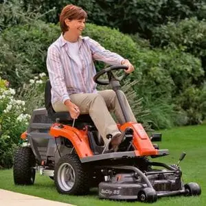 a smiling woman mowing a lawn, using the Husqvarna Small Ride On Out-Front Lawn Mower R 112C