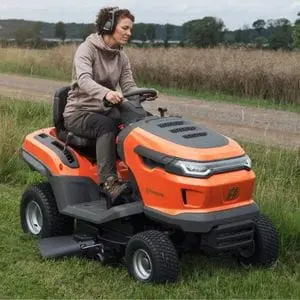 a woman wearing ear defenders, cutting grass using the Husqvarna TS 215T Garden Tractor