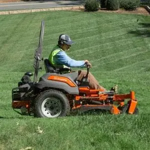 a man wearing a high-visibility jacket, baseball cap and ear defenders, mowing grass on a hill using the Husqvarna Z560X Zero Turn Mower