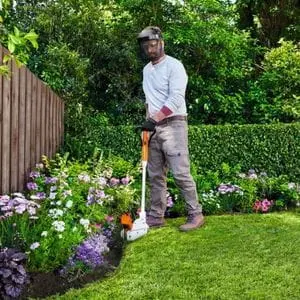 a man wearing a face shield and gloves, using the STIHL FSA 30 Cordless Grass Trimmer to cut a lawn edge, where it meets a flower bed