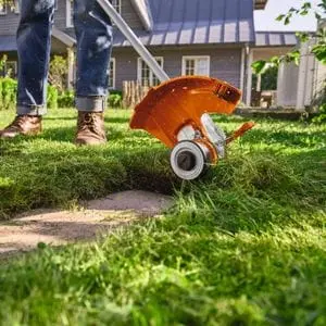 someone using the STIHL FSA 50 Cordless Grass Trimmer to cut around a small concrete square on a lawn