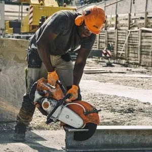 a man wearing a hardhat and ear defenders, using the STIHL TS 500i Petrol Cut-off Machine to cut a concrete girder on a building site