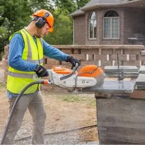 a man wearing a hardhat and ear defenders, using the STIHL TSA 300 Cordless Cut-off Machine to cut slabs outside a house