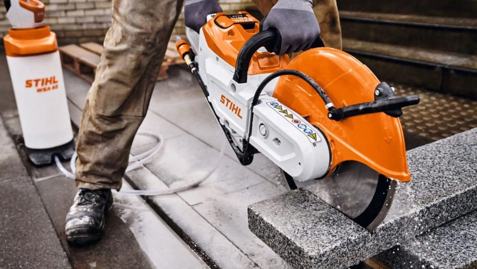 a close up of someone cutting concrete blocks using the STIHL TSA 350 Cordless Cut-off Machine, with a STIHL Pressurised Water Container in the background