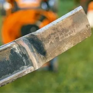 a close up of a lawn mower blade, with an orange mower in the background