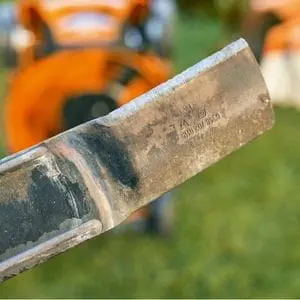 a close up of a STIHL lawn mower blade, with an orange lawn mower in the background