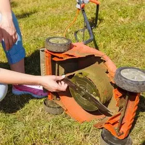 a woman examining the blade on an orange lawnmower