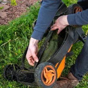 a man examining the blade on an upturned lawn mower