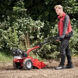 a man using the AL-KO COMBI BF 5002-R Two Wheel Tractor to cultivate soil at the edge of a field