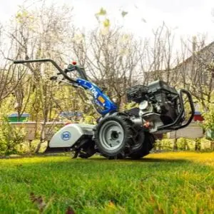 the BCS 706 Petrol Rotavator parked on a lawn, near some trees and houses
