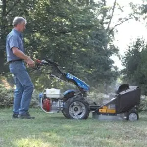 a man using the BCS 706 Petrol Rotavator with Single Blade Lawn Mower to cut grass in a garden