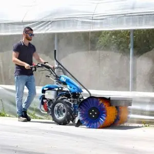 a man using the BCS 738 Two Wheel Tractor with a brush attachment to clean a path next to a large marquee