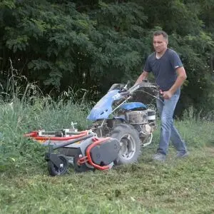 a man cutting long grass at the edge of a field using the BCS 738 Two Wheel Tractor