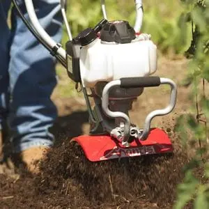a close up of someone cultivating soil using the Mantis 7265-12-14 Petrol Tiller