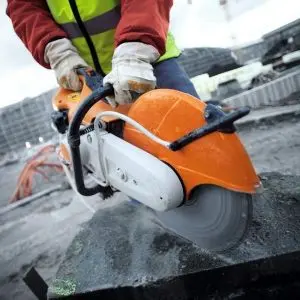 Close-up of a construction worker wearing protective gloves and a high-visibility vest using a STIHL TS 410 Petrol Cut-Off Machine to cut a concrete slab on a building site.