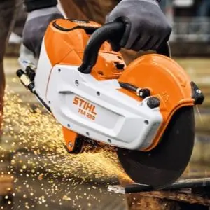 Close-up of a worker wearing protective gloves using a STIHL TSA 230 Cordless Cut-Off Machine to cut metal, with sparks flying from the cutting wheel.