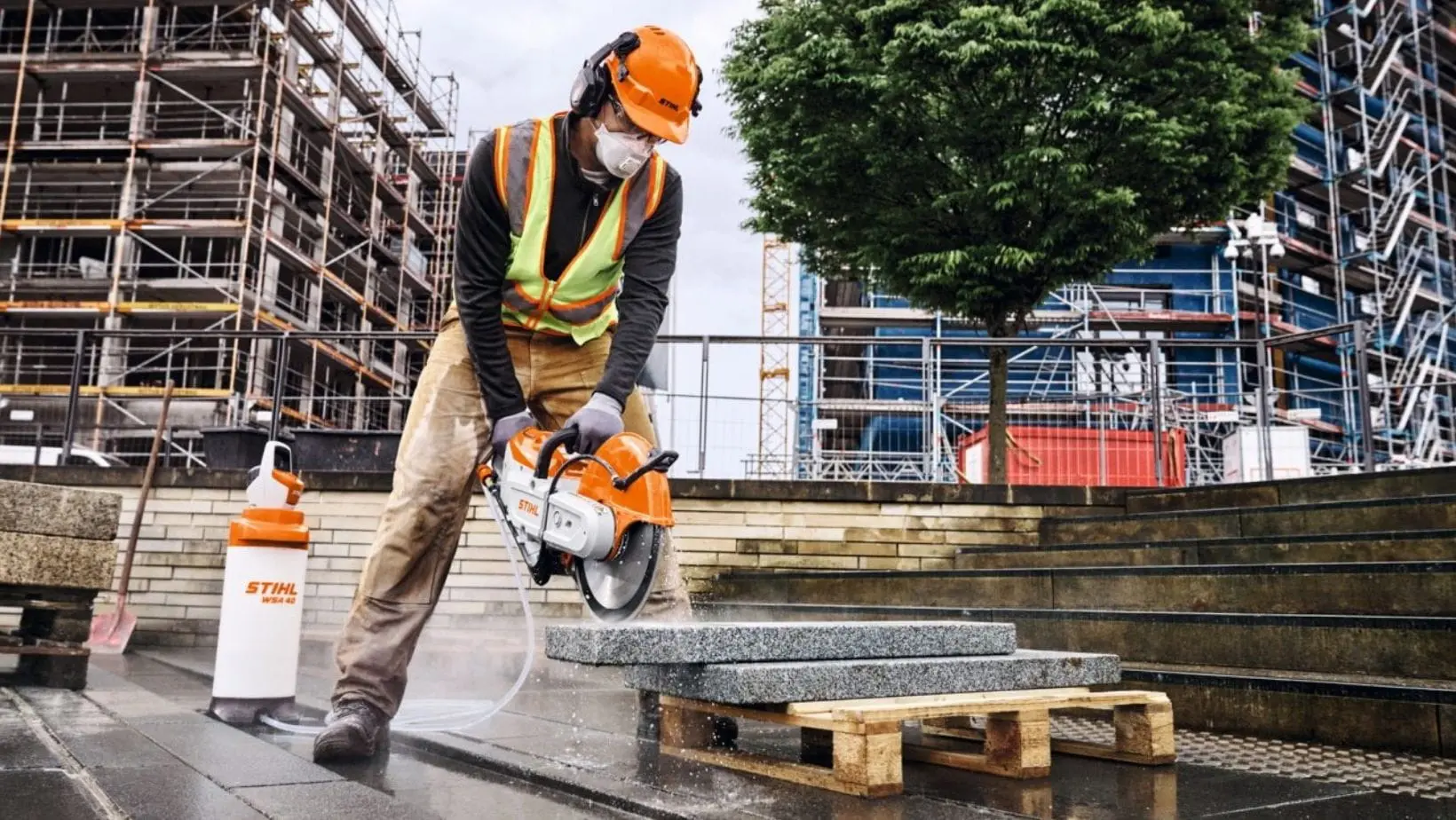 STIHL TSA 350 Cordless Cut-off Machine (1) a man wearing hardhat, ear defenders and dust mask, using the STIHL TSA 350 Cordless Cut-off Machine with STIHL WSA 40 Cordless Pressurised Water Container to cut slabs on a construction site