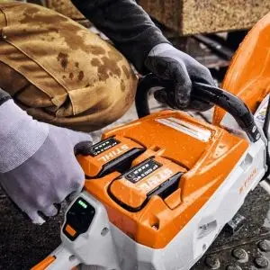 Close-up of a worker wearing protective gloves operating the controls of a STIHL TSA 500 Cordless Cut-Off Machine, with the orange housing and battery compartment clearly visible.